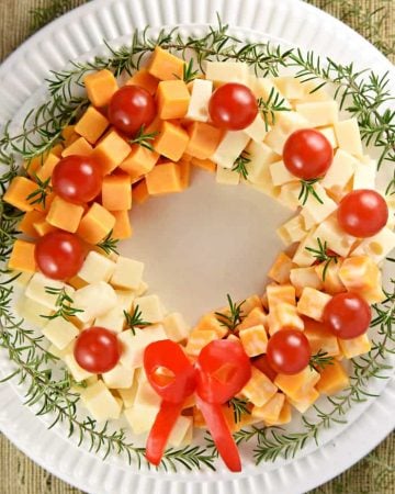 Holiday Cheese Wreath ~ this easy and festive Christmas party appetizer is made by arranging cubes of cheese in a ring, accenting with cherry tomatoes and a garland of rosemary, and finishing off with a bell pepper bow! | FIveHeartHome.com