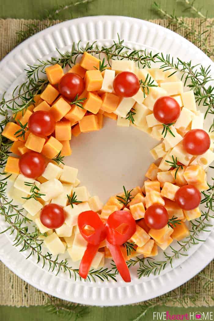 Holiday Cheese Wreath ~ this easy and festive Christmas party appetizer is made by arranging cubes of cheese in a ring, accenting with cherry tomatoes and a garland of rosemary, and finishing off with a bell pepper bow! | FIveHeartHome.com
