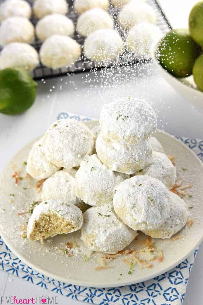 Lime Coconut Snowball Cookies ~ tender, shortbread-like cookies studded with lime zest & toasted coconut and generously rolled in powdered sugar for yummy year-round treats…from the lazy days of summer to a Christmas cookie platter! | FiveHeartHome.com Plate of Snowball Cookies being showered with powdered sugar.