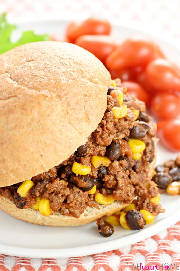 Close-up of sandwich on plate with ground beef, black beans, and corn spilling out of the bun