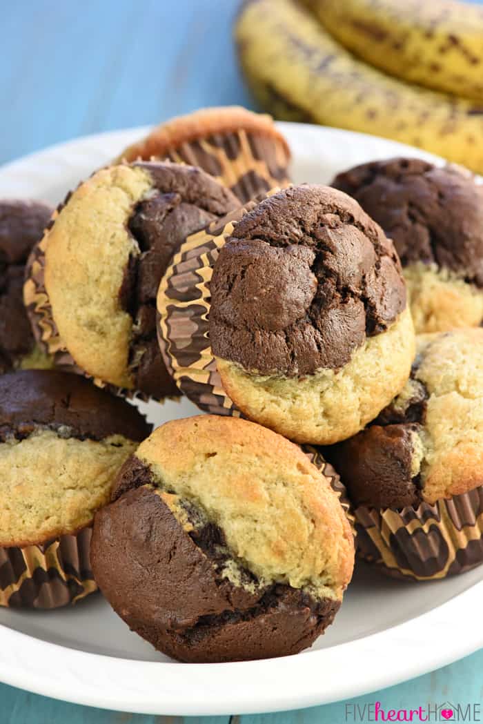 Chocolate Banana Muffins ~ combine half plain banana batter and half chocolate banana batter in sweet, moist, bakery-style muffins that make a perfect breakfast or snack! | FiveHeartHome.com Chocolate Banana Muffins piled in a heap on white platter