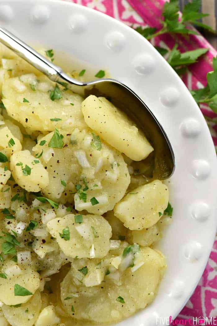 Aerial close-up of Kartoffelsalat with onions and parsley in dish with spoon.