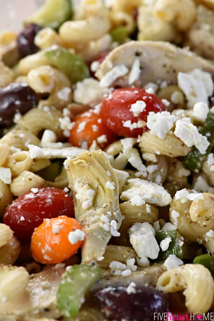 Zoomed shot of ingredients in Greek Pasta Salad, including chicken, artichokes, tomatoes, olives, and feta