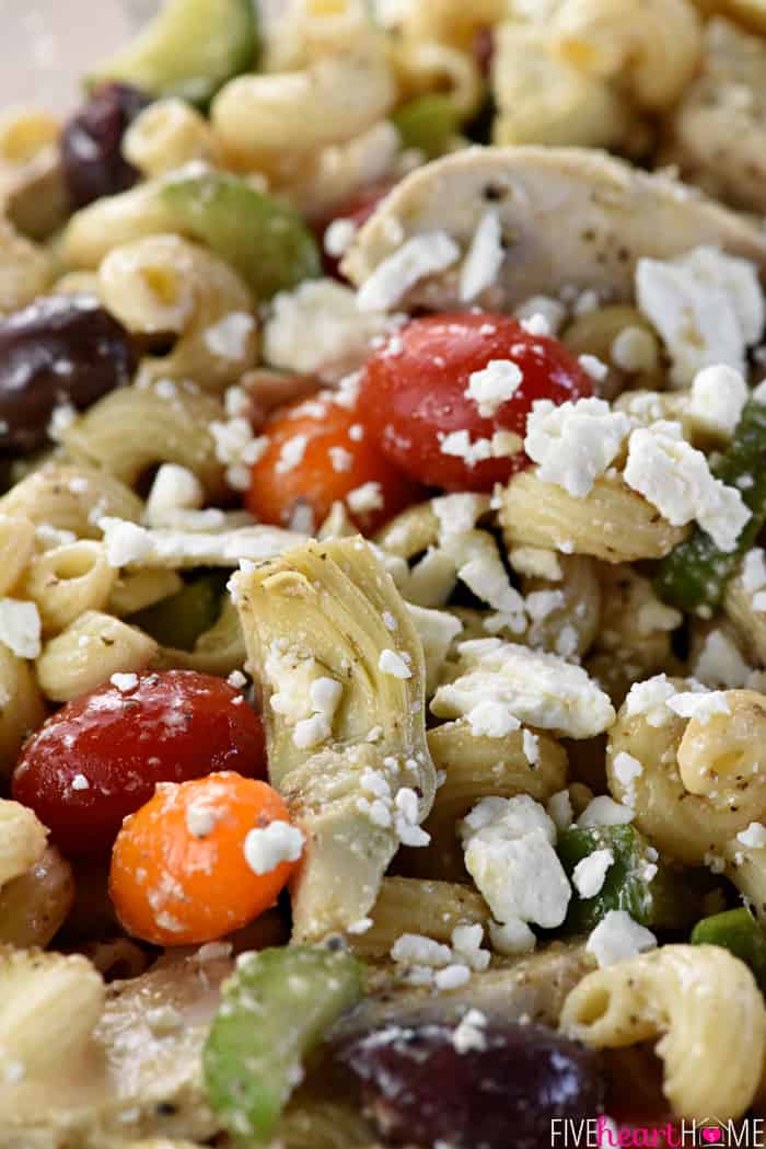 Zoomed shot of ingredients in Greek Pasta Salad, including chicken, artichokes, tomatoes, olives, and feta