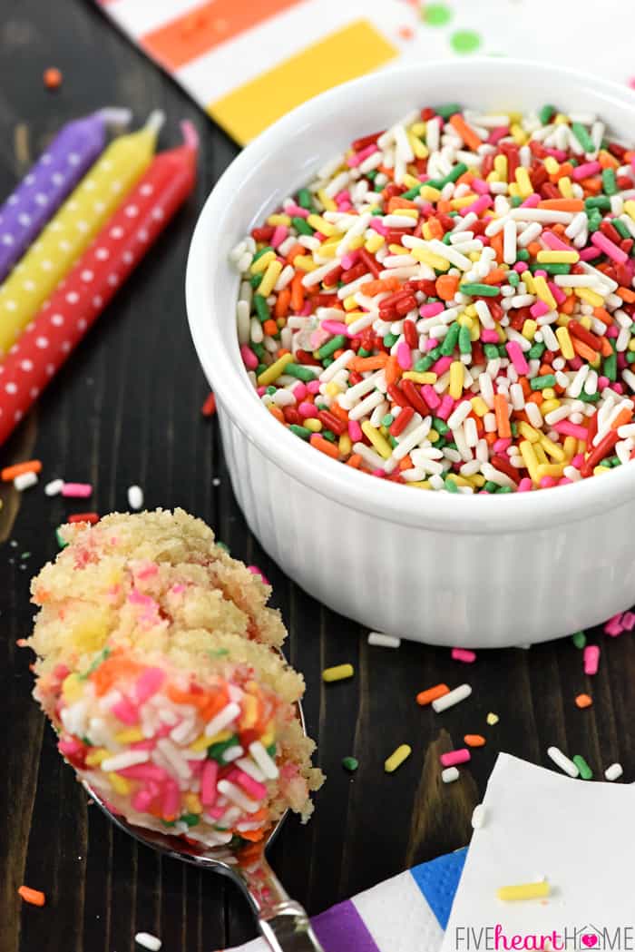 White dish full of colorful sprinkles, with candles and birthday napkins on the table