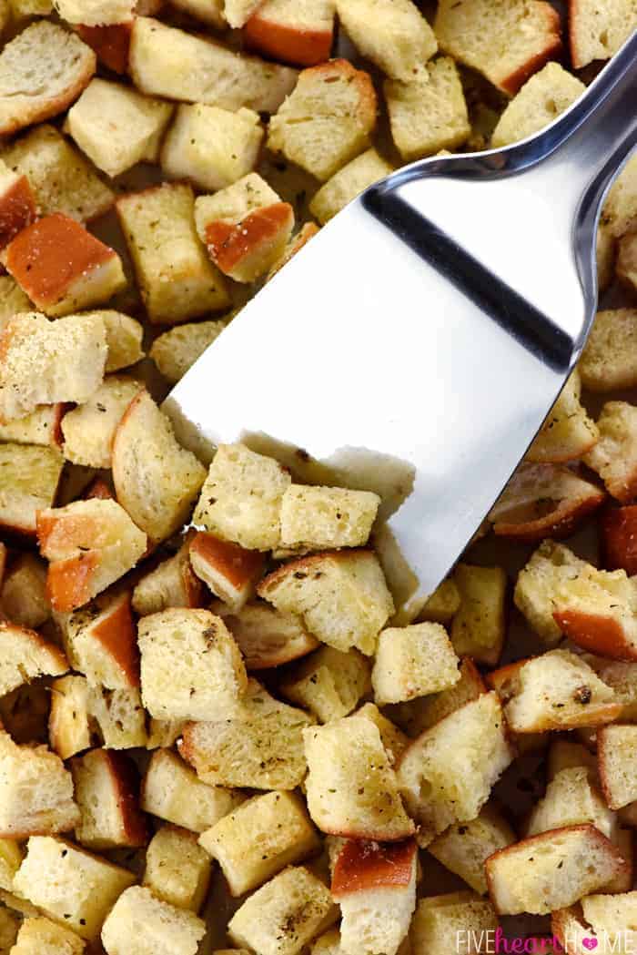 Aerial view of metal spatula stirring Homemade Croutons on pan.