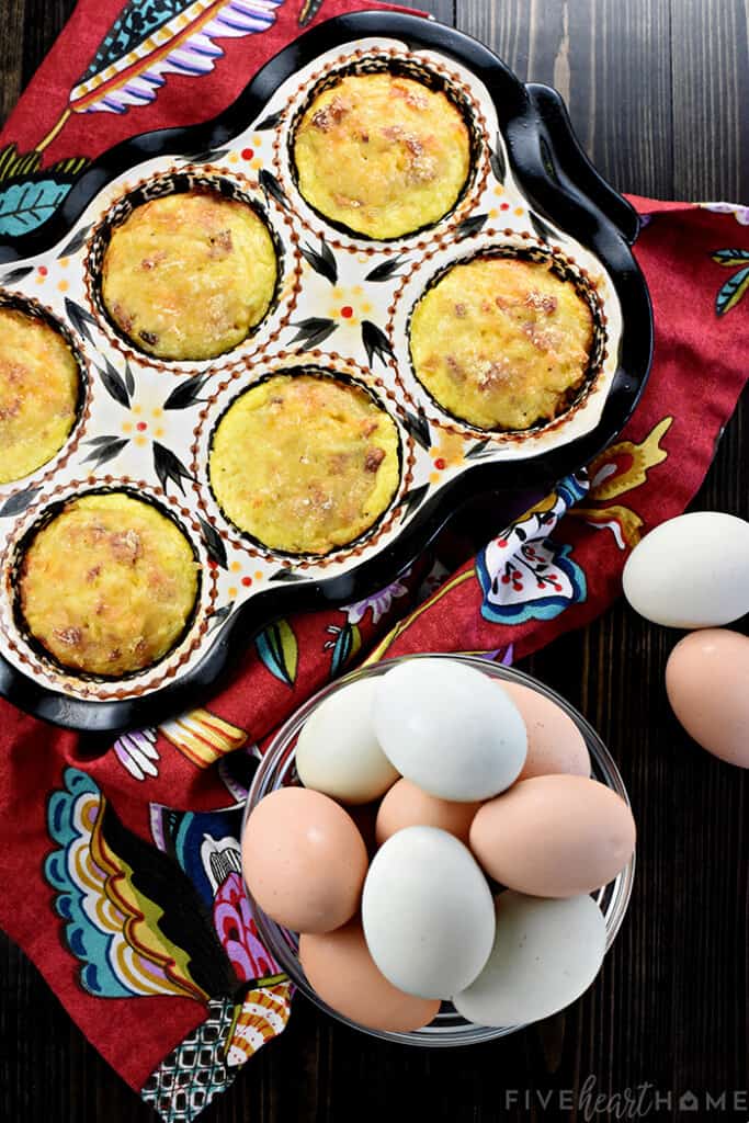 Aerial view of Mini Frittatas in pan with bowl of fresh eggs on table.