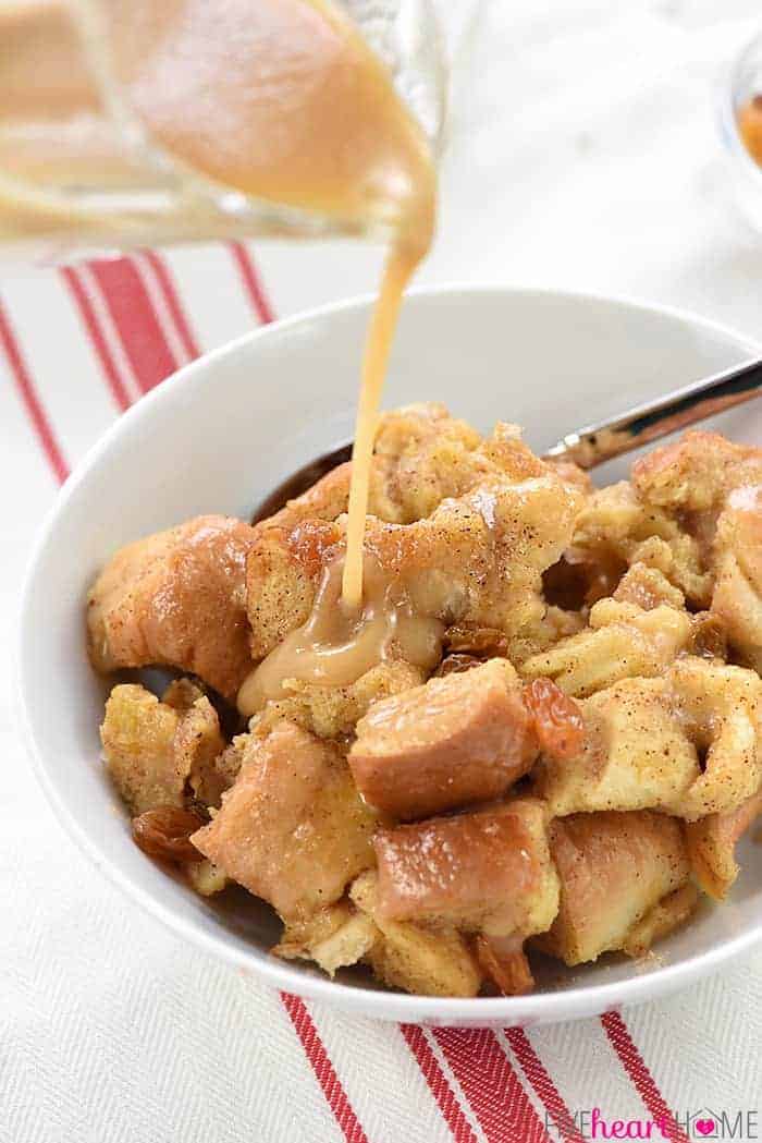 Slow Cooker Eggnog Bread Pudding ~ this decadent holiday breakfast, brunch, or dessert is studded with golden raisins, sprinkled with nutmeg, and drizzled with a silky eggnog syrup...and it effortlessly cooks up in the crock pot, freeing up the oven for other recipes! | FiveHeartHome.com In White Bowl with Sauce Being Poured On Top Of