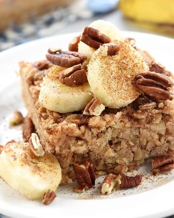 Banana Baked Oatmeal on a plate garnished with sliced bananas, toasted pecans, and cinnamon