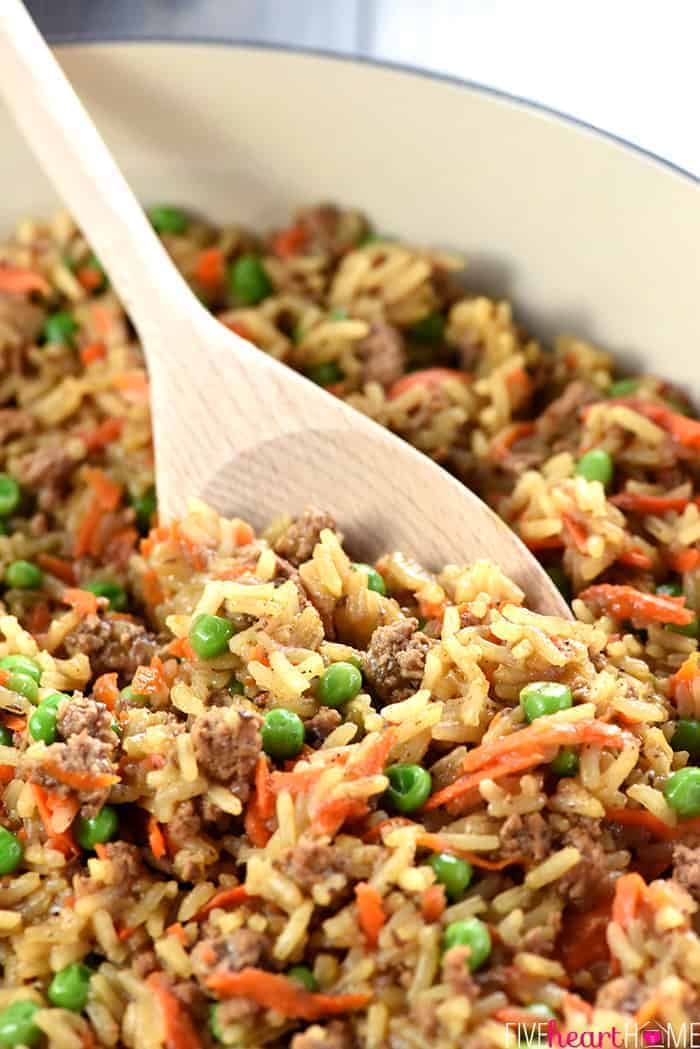 Close-up of wooden spooning dipping into ground beef and rice recipe.