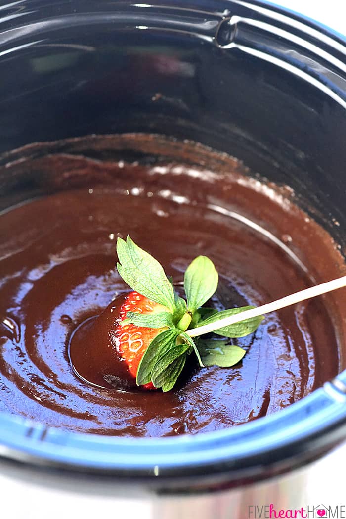 Slow Cooker Chocolate Peanut Butter Fondue ~ a decadent, glossy, chocolate dessert recipe kissed with peanut butter, the perfect crock pot dip for your favorite fruit and confections on Valentine's Day or any day! | FiveHeartHome.com Strawberry being dunked in Slow Cooker Chocolate Peanut Butter Fondue.