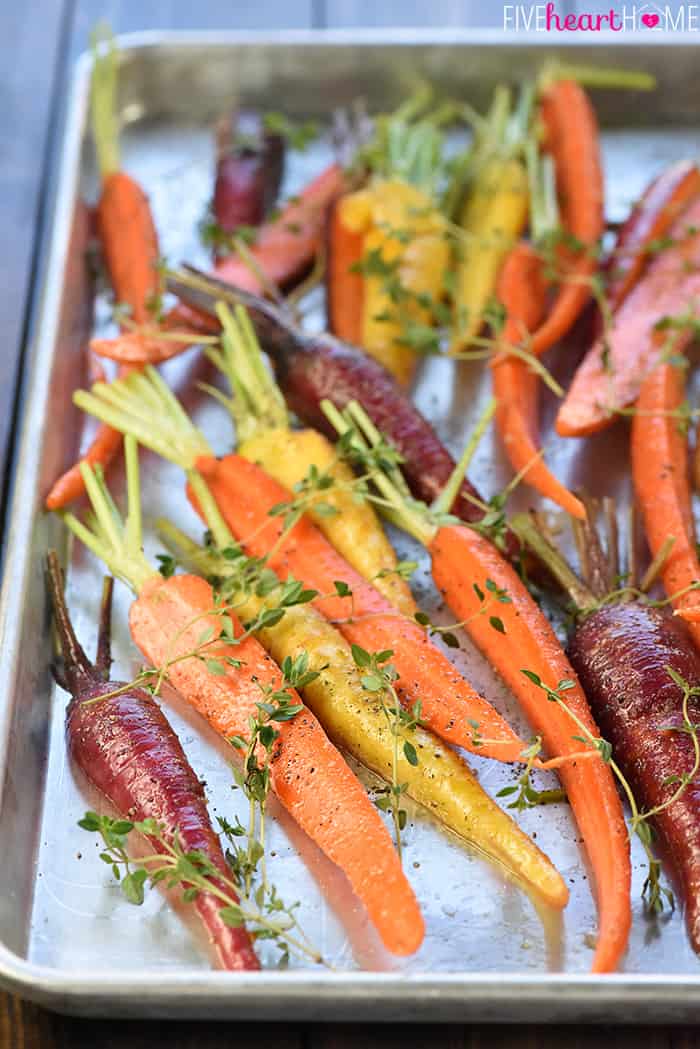 Rainbow carrots and fresh thyme on baking sheet.