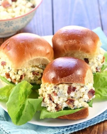 Egg Salad sandwiches with bacon and blue cheese on plate with lettuce.