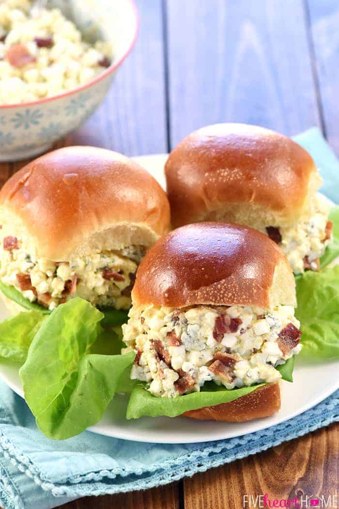 Egg Salad sandwiches with bacon and blue cheese on plate with lettuce.