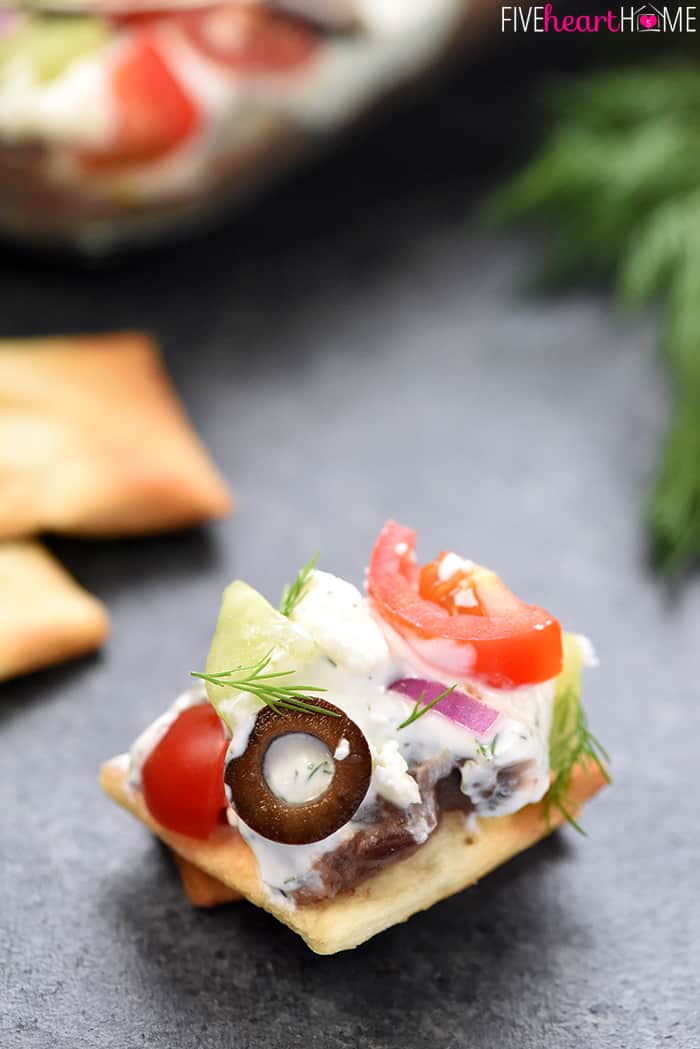 Greek 7-Layer Dip ~ a Mediterranean spin on the beloved, classic recipe, with layers of hummus, dill-infused Greek yogurt, tomatoes, cucumbers, black olives, red onion, and feta cheese! | FiveHeartHome.com Scoop on a pita chip.
