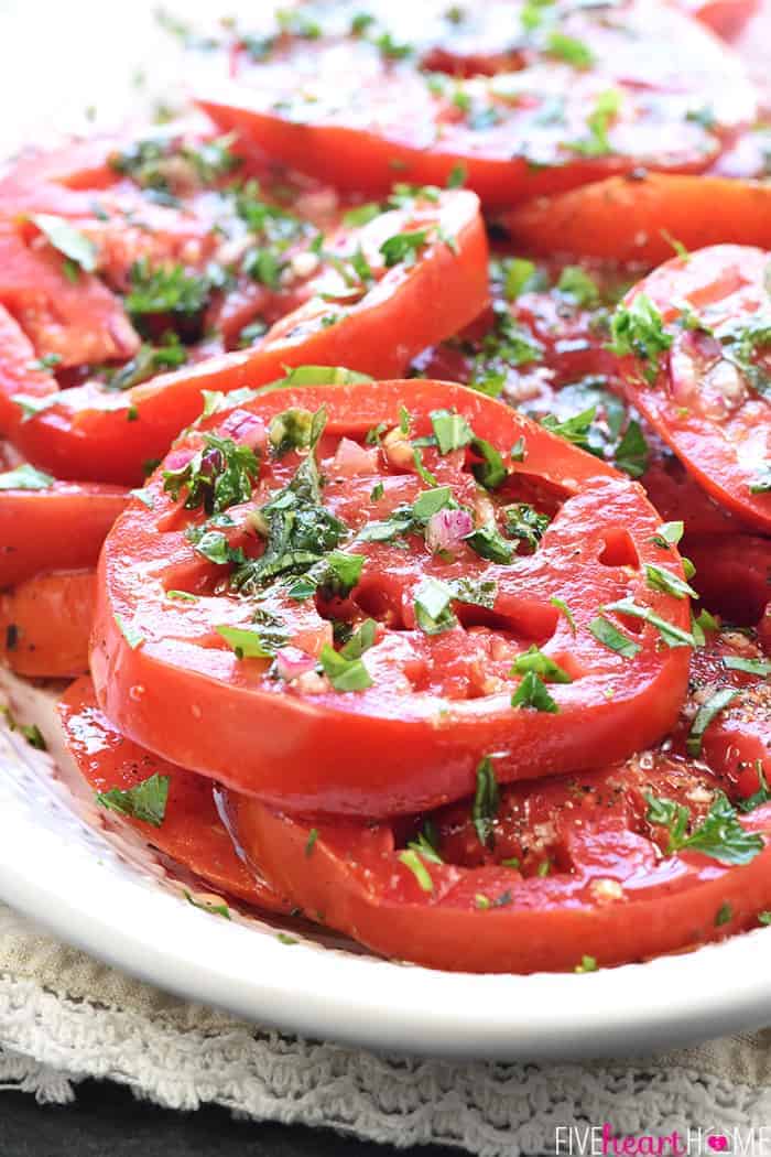 Close-up of sliced marinated tomatoes garnished with herbs.