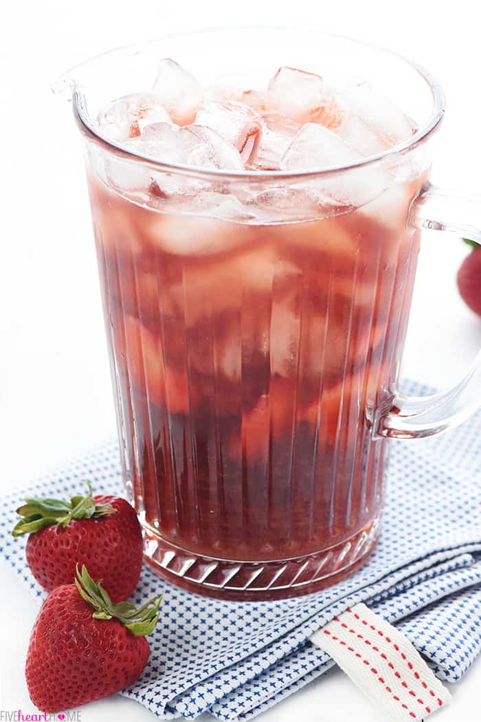 Strawberry Iced Tea ~ made with sweet, fresh, strawberry simple syrup for a refreshing summer drink! | FiveHeartHome.com Full pitcher on a folded blue and white towel with strawberries sitting on table
