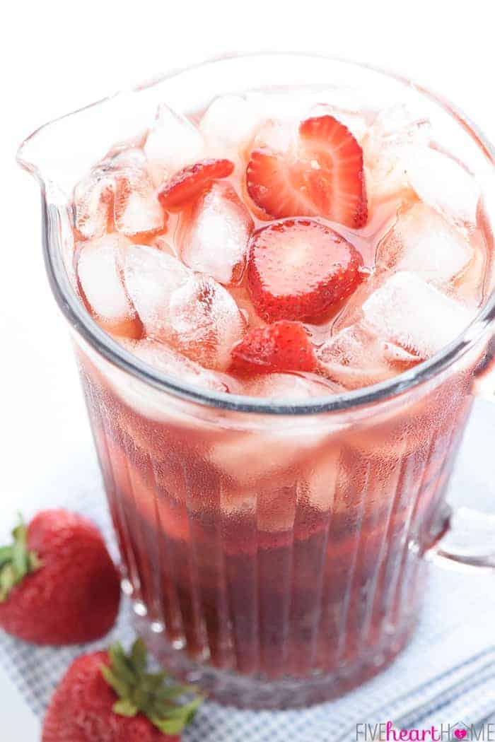 Strawberry Iced Tea in a pitcher, filled with ice and sliced strawberries