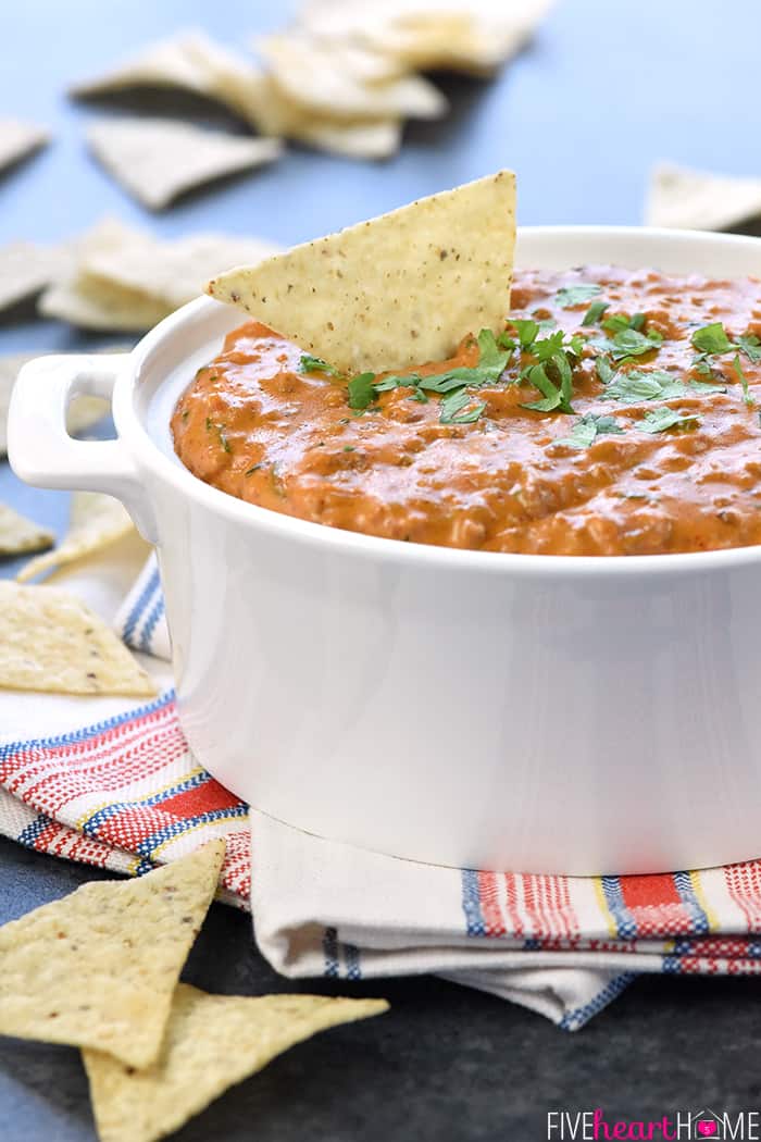 Hot Taco Dip in white serving dish with tortillla chip dipping into it.