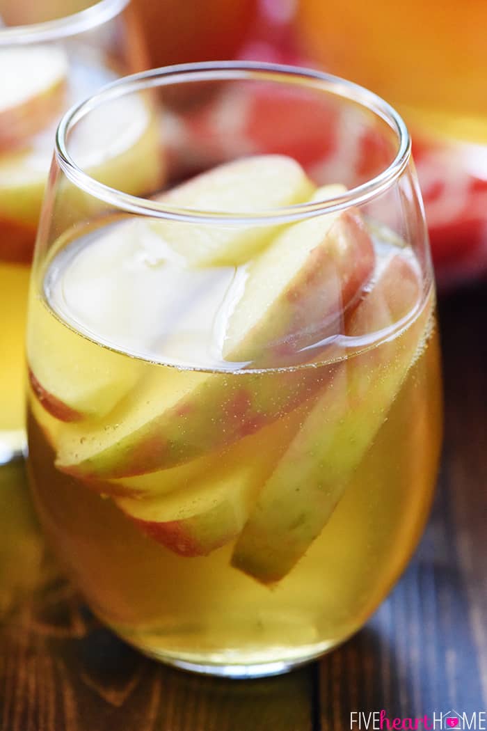Sparkling Apple Cider Sangria ~ a festive fall cocktail recipe with just three ingredients -- white wine, apple cider, and sweet sliced Honeycrisps -- perfect for tailgating, Halloween, Thanksgiving, and even Christmas! | FiveHeartHome.com Apple Cider Sangria in a glass with floating Honeycrisp slices