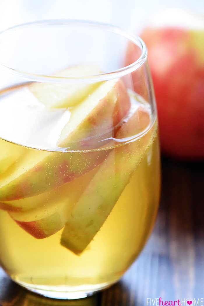Sparkling Apple Cider Sangria ~ a festive fall cocktail recipe with just three ingredients -- white wine, apple cider, and sweet sliced Honeycrisps -- perfect for tailgating, Halloween, Thanksgiving, and even Christmas! | FiveHeartHome.com Close up of apple slices floating in glass