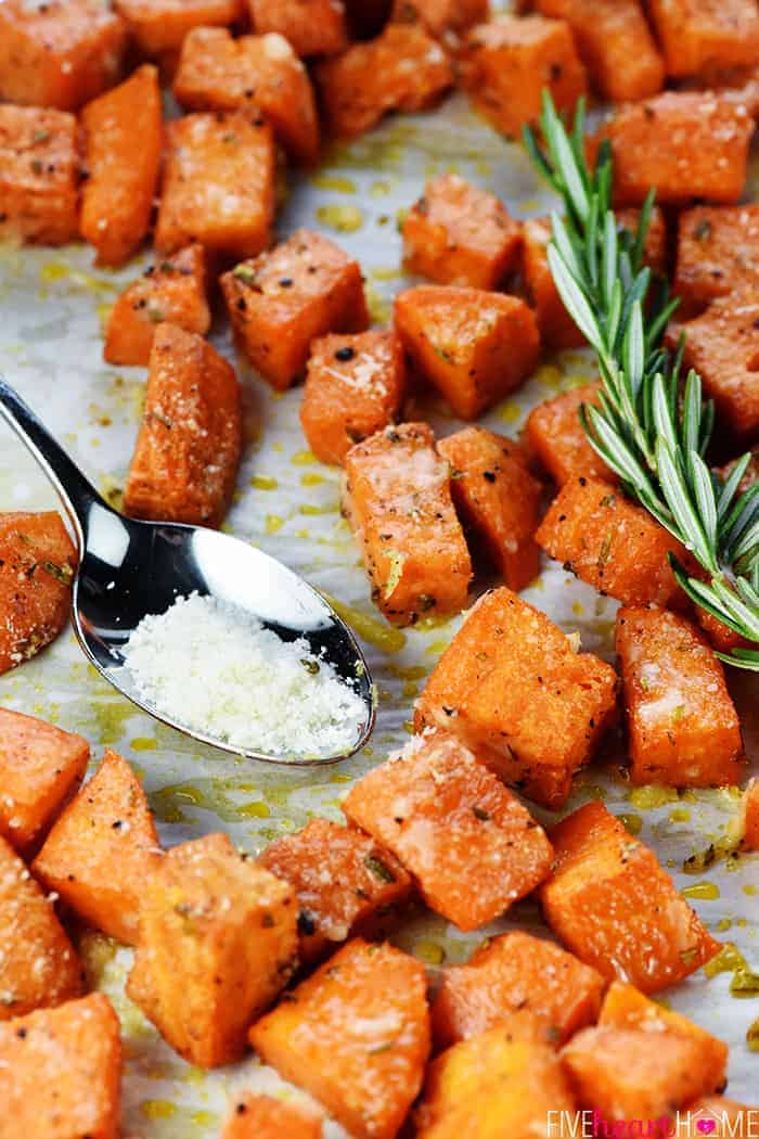 Savory Sweet Potatoes on baking sheet with sprig of rosemary and spoonful of Parmesan.