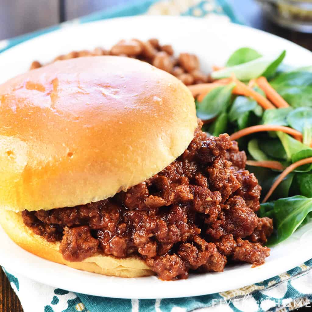 Closeup of Sloppy Joe recipe that's easy and the best, made with a homemade sloppy joe sauce, piled on a bun on a plate with sides.