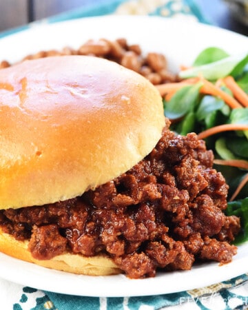 Closeup of Sloppy Joe recipe that's easy and the best, made with a homemade sloppy joe sauce, piled on a bun on a plate with sides.