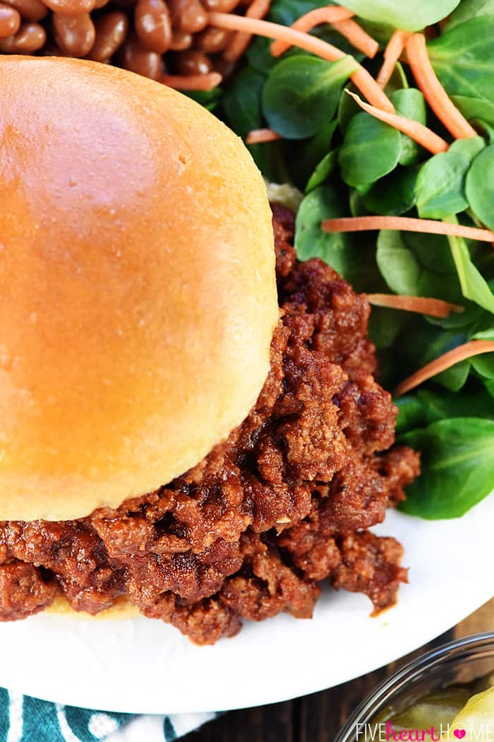 Aerial view of Sloppy Joe recipe piled on bun on plate with beans and salad.