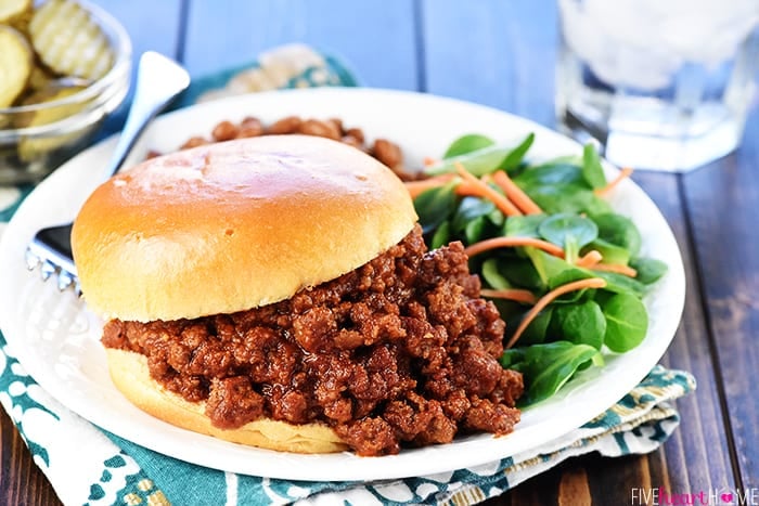 Sloppy Joes sandwich on a plate with beans and salad.