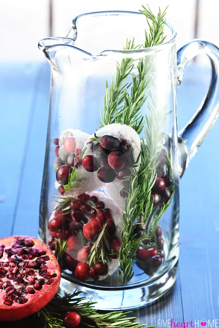 Easy Christmas Punch ~ a festive, sparkling, boozy holiday beverage featuring champagne, pomegranate juice, and cranberry juice that's perfect for Christmas or New Year's Eve parties...and it's easy to make a non-alcoholic version as well! | FiveHeartHome.com Glass pitcher with ice cubes and garnishes.