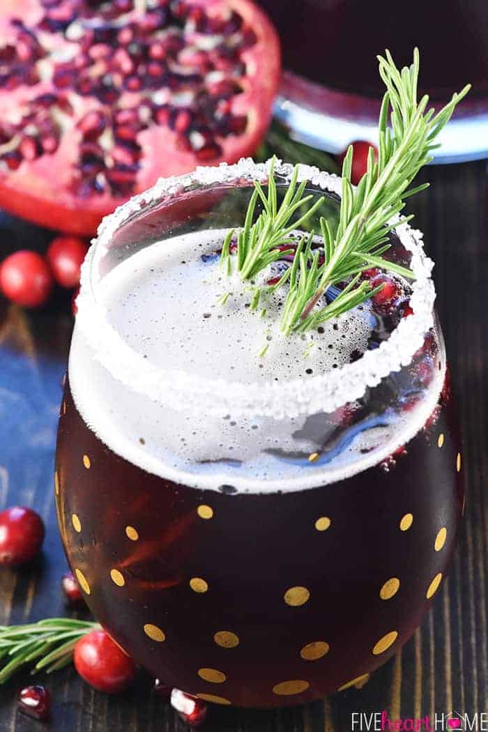 Easy Christmas Punch ~ a festive, sparkling, boozy holiday beverage featuring champagne, pomegranate juice, and cranberry juice that's perfect for Christmas or New Year's Eve parties...and it's easy to make a non-alcoholic version as well! | FiveHeartHome.com Christmas Punch in glass with sugar rim and rosemary sprig.