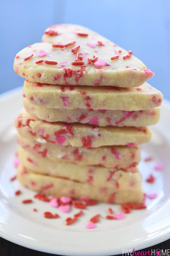 Stack of heart cookies on a plate with sprinkles.