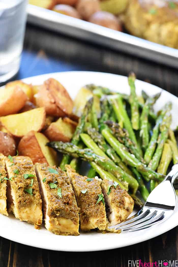 Sliced pesto chicken on plate along with roasted potatoes and asparagus.