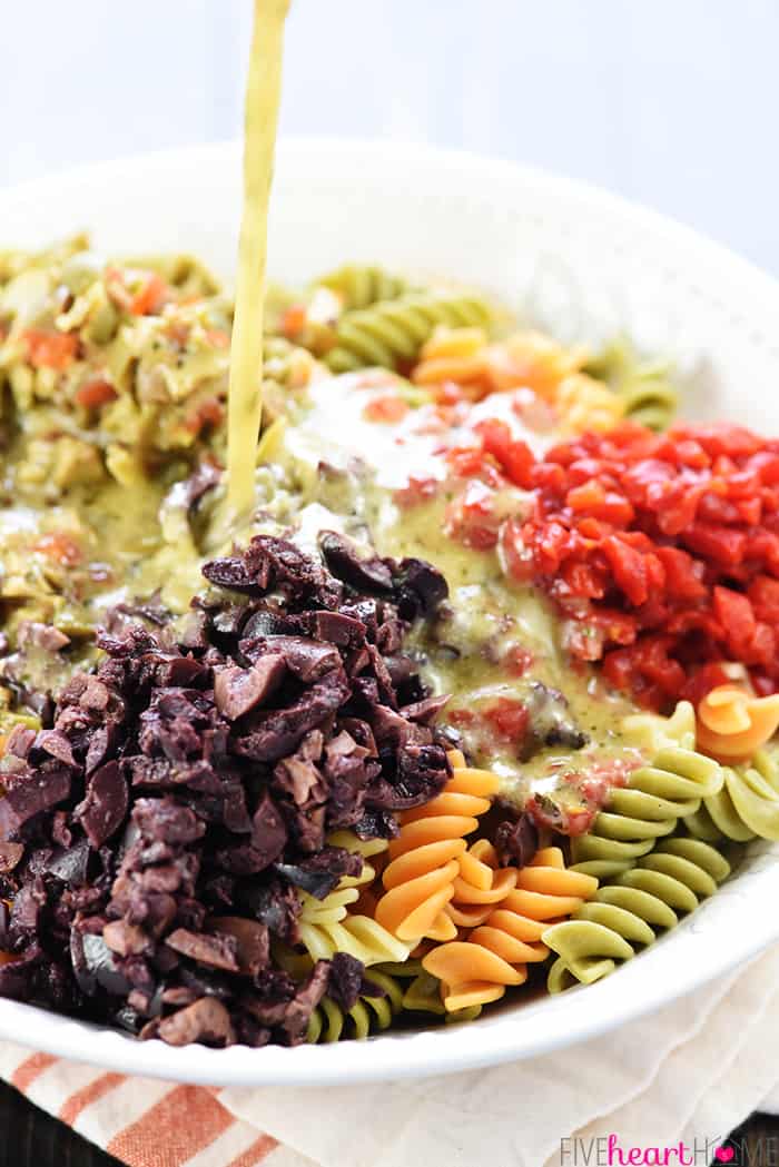 Easy Pasta Salad ~ tri-color garden rotini is studded with diced olives and pimentos, tossed with a zesty homemade Italian dressing, and showered with Parmesan for a versatile summer side dish recipe! | FiveHeartHome.com Pasta salad with Italian dressing being poured on.
