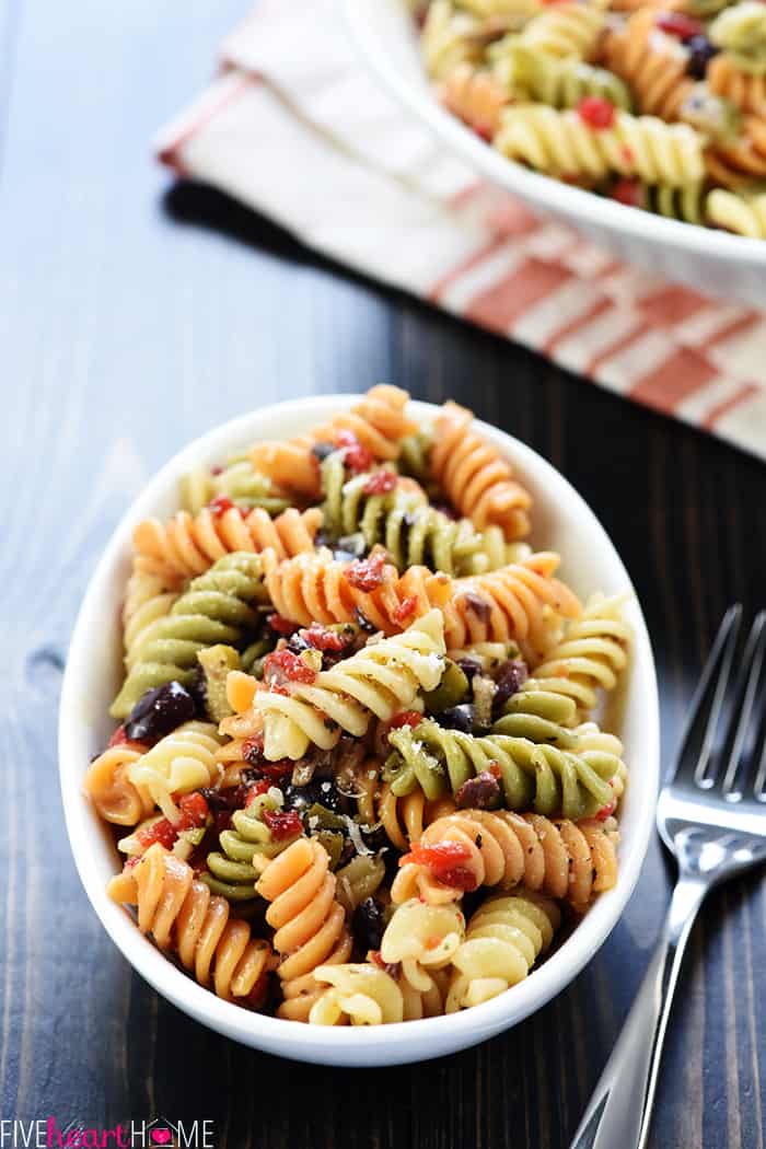 Easy Pasta Salad ~ tri-color garden rotini is studded with diced olives and pimentos, tossed with a zesty homemade Italian dressing, and showered with Parmesan for a versatile summer side dish recipe! | FiveHeartHome.com In a serving dish with a fork.