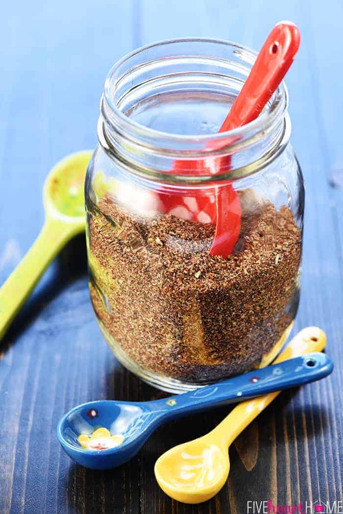 Mason jar of Taco Seasoning with colorful ceramic measuring spoons.