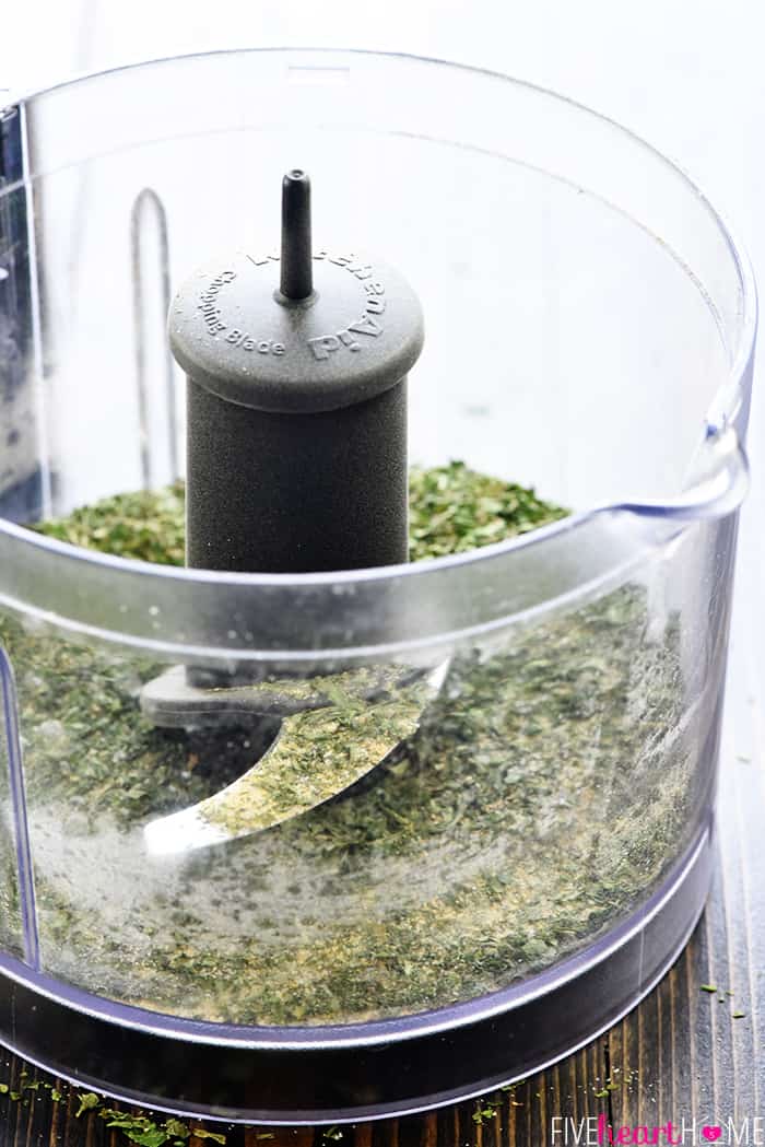 Dried herbs and other ingredients being pulsed in a food processor.