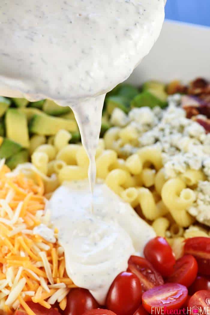 Ranch dressing being poured over Cobb Pasta Salad.