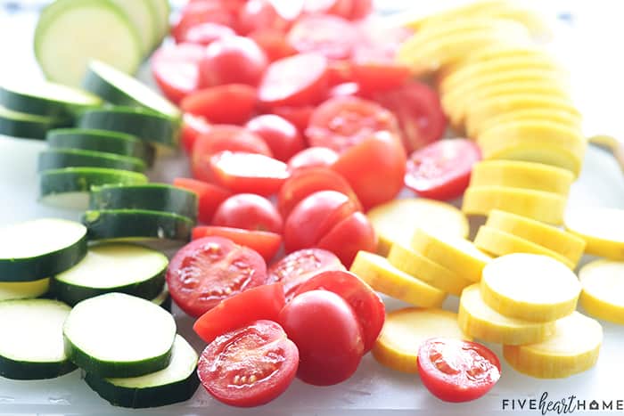 Sliced zucchini, tomatoes, and yellow squash on cutting board.