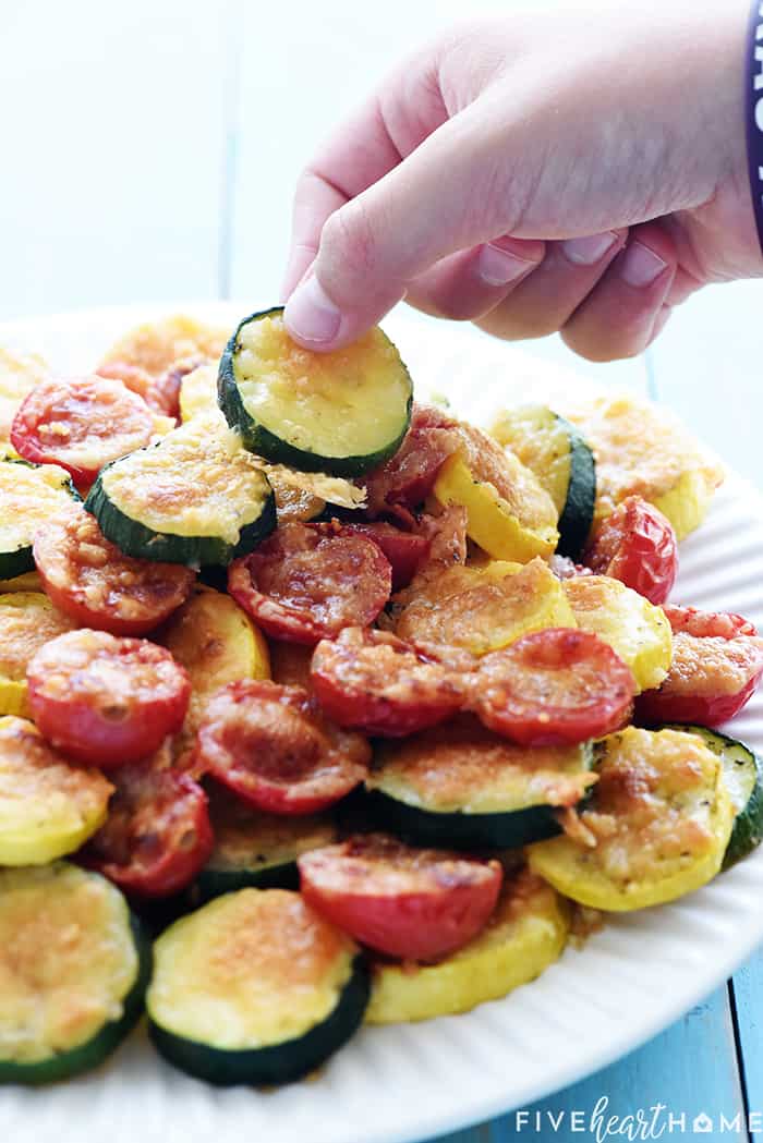 Child's hand stealing a piece of zucchini from plate.