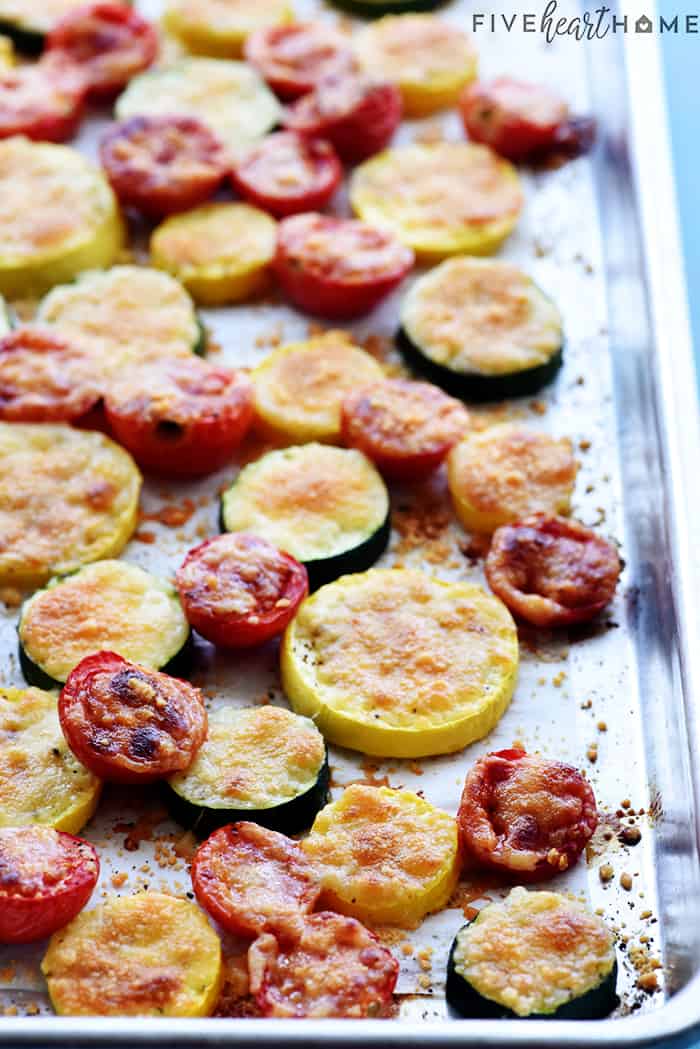 Zucchini, squash, and tomatoes topped with melted parmesan on baking sheet.