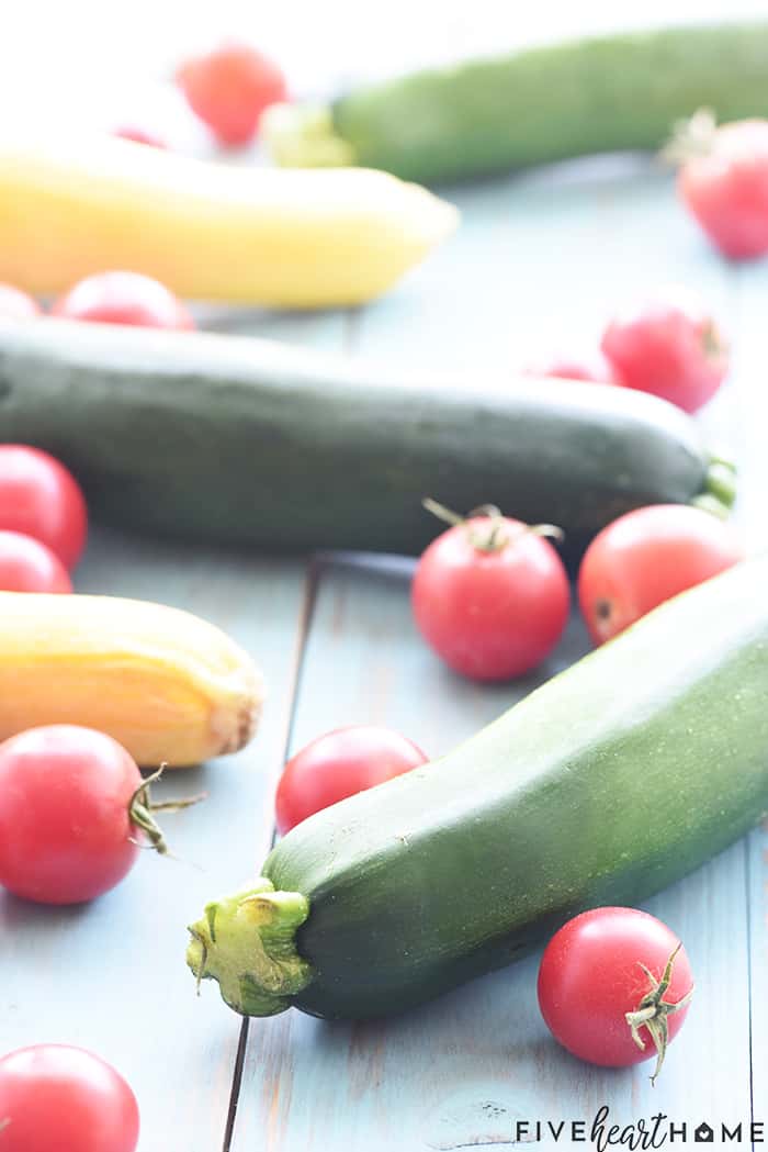 Summer vegetables, including zucchini, yellow squash, and tomatoes, on blue table.