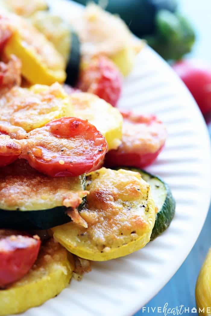 Close-up of melted parmesan over slices of zucchini, squash, and tomatoes.