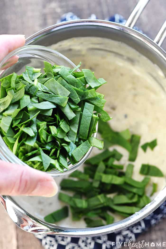 Chopped spinach being added to pot of white queso.