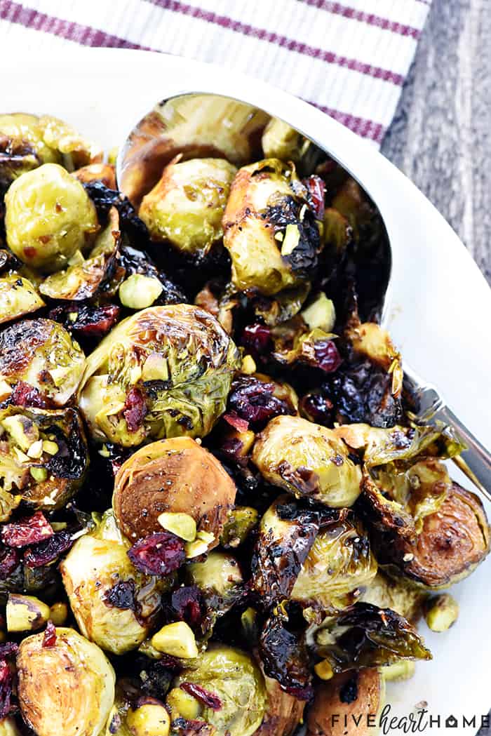 Roasted Brussel Sprouts with Balsamic, Pistachios, and Cranberries on platter with spoon.