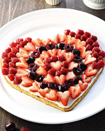 Valentine's Day Fruit Pizza ~ featuring a tangy cream cheese frosting on a heart-shaped sugar cookie crust topped by sweet, glossy berries and cherries, this is the perfect Valentine's Day dessert recipe! | FiveHeartHome.com
