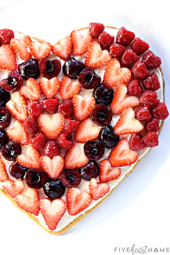 Valentine's Day Fruit Pizza ~ featuring a tangy cream cheese frosting on a heart-shaped sugar cookie crust topped by sweet, glossy berries and cherries, this is the perfect Valentine's Day dessert recipe! | FiveHeartHome.com