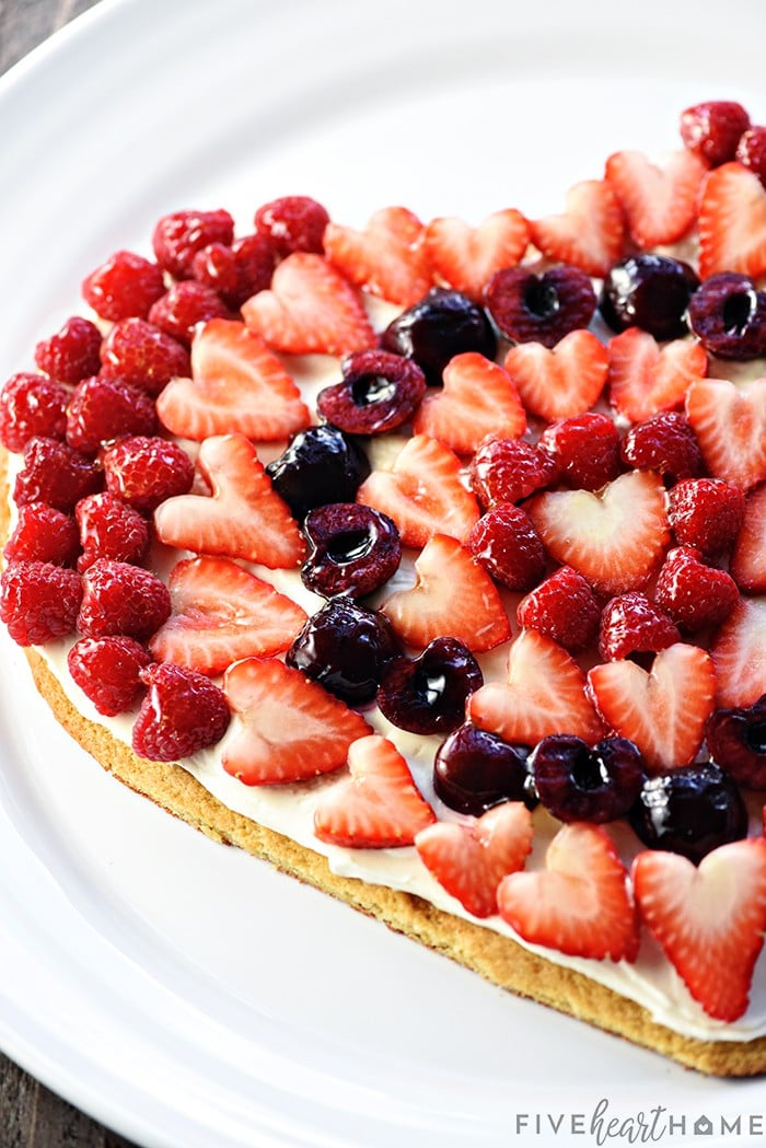 Fruit Pizza ~ on a heart-shaped sugar cookie crust, this fruit pizza features cream cheese frosting topped by glossy berries & cherries. It's a perfect Valentine's Day dessert or treat for any occasion! | FiveHeartHome.com.com Fruit Pizza on a white serving platter.