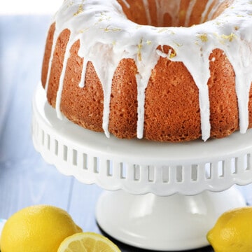 Homemade Lemon Pound Cake on cake stand with fresh lemons on table.
